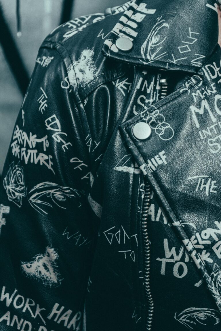 Close-up of a stylish black leather jacket featuring bold graffiti-style text and graphics.