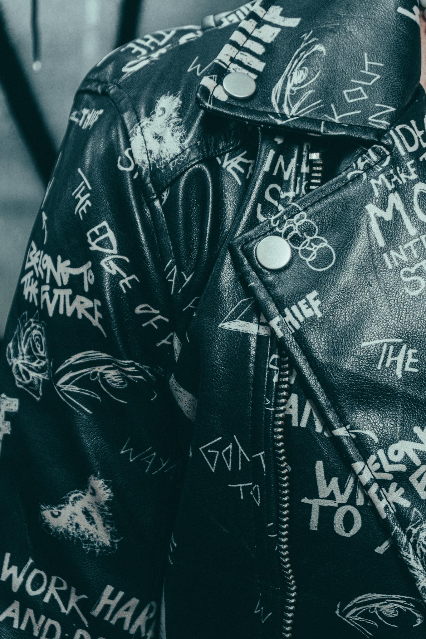 Close-up of a stylish black leather jacket featuring bold graffiti-style text and graphics.