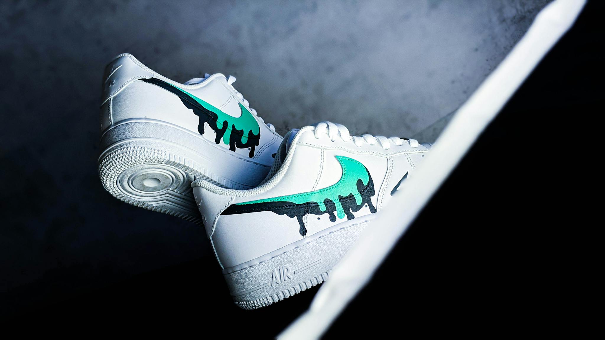 Close-up of trendy white sneakers featuring a unique teal swoosh design on a gray background.