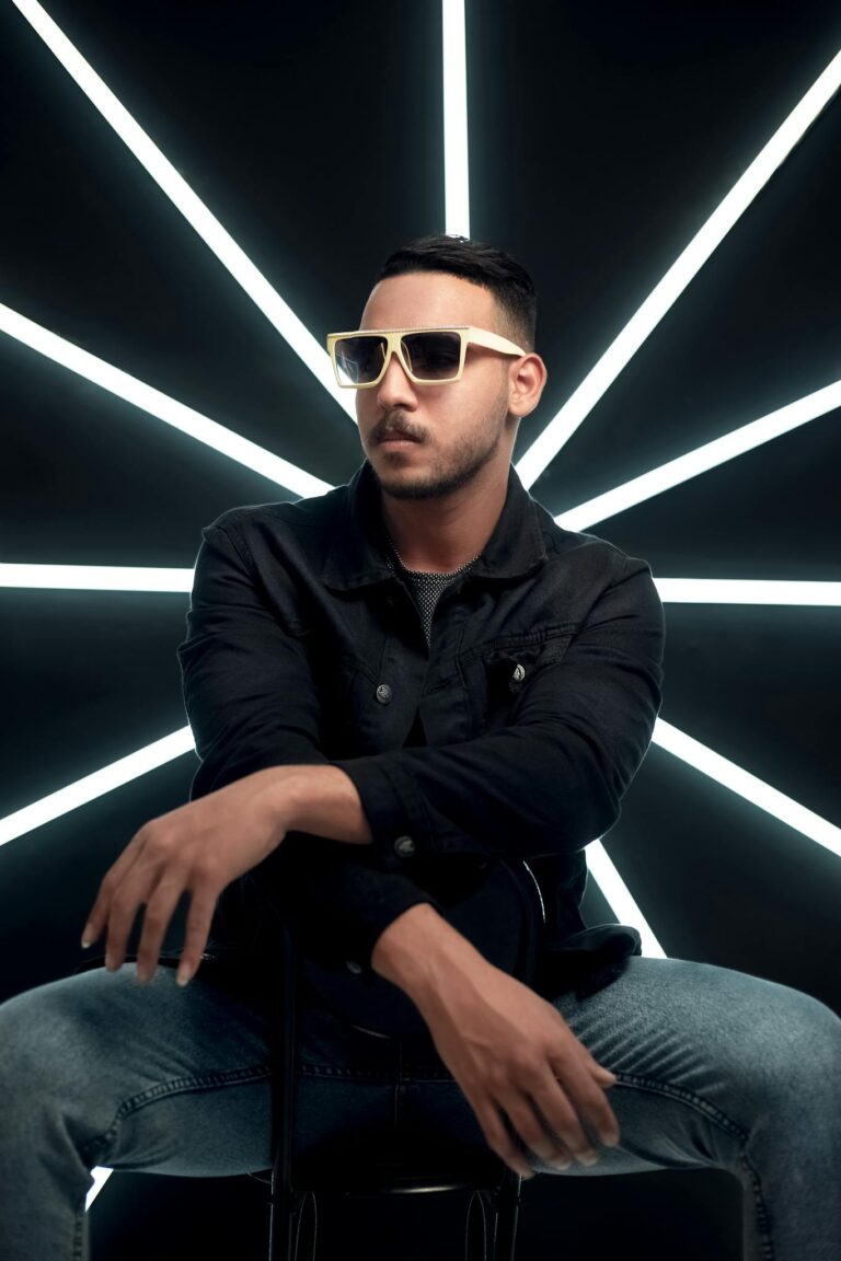 Fashionable man in sunglasses posing in a studio with striking LED light backdrop.